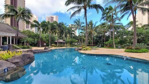 A swimming pool surrounded by palm trees and a building with a tiled roof. - Marbella Lane- Prime Watermark Ocean & City View (Honolulu)