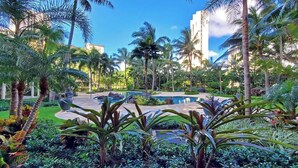 A tropical resort with a pool surrounded by palm trees and lush greenery. - Marbella Lane- Prime Watermark Ocean & City View (Honolulu)