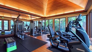 A gym with various exercise equipment, large windows, and a wooden ceiling. - Marbella Lane- Prime Watermark Ocean & City View (Honolulu)