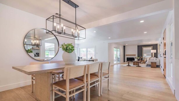 Un comedor amplio con una mesa y sillas de madera, un espejo redondo y una lámpara colgante moderna.