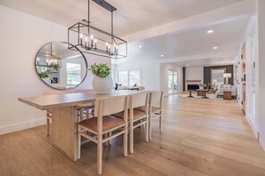 A spacious dining area with a wooden table and chairs, a round mirror, and a modern pendant light. - Cozy Modern Haven w/ Soothing Ambience & Pool (Fullerton)