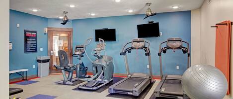 Ein Fitnessstudio mit Laufbändern, Crosstrainern und einem großen Trainingsball.