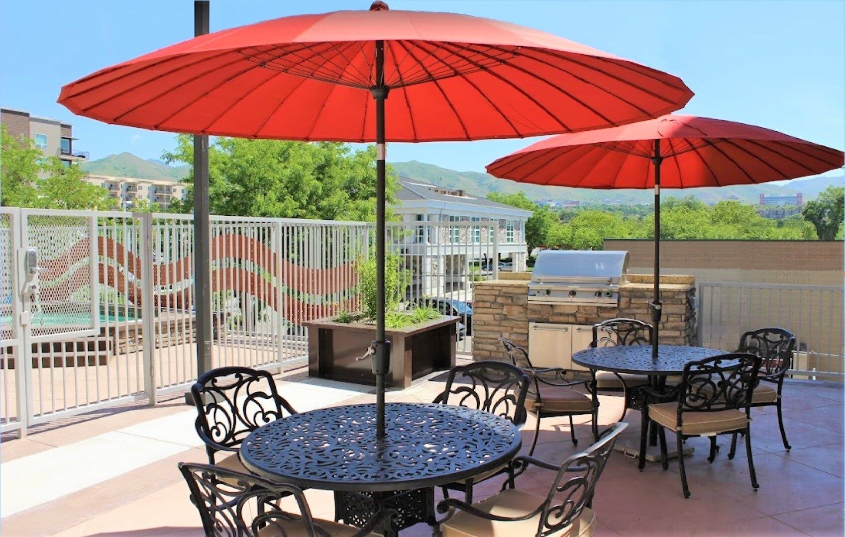 Une terrasse extérieure avec deux tables rondes, quatre chaises et deux parasols rouges.