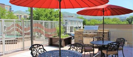 Une terrasse extérieure avec deux tables rondes, quatre chaises et deux parasols rouges.