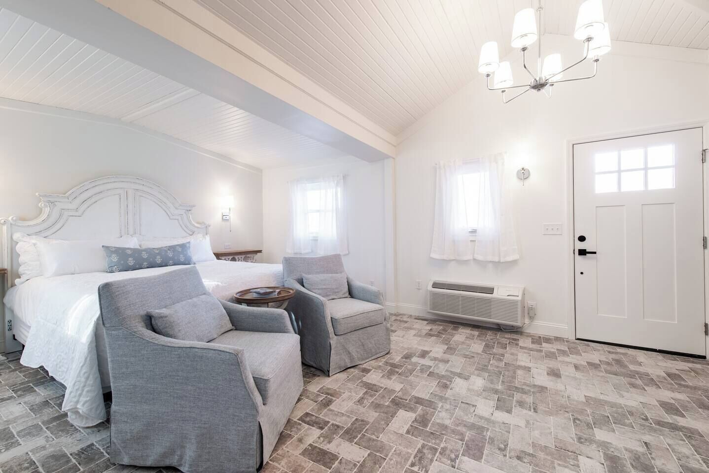 Un dormitorio con una cama, dos sillones, una mesita y un radiador, además de una puerta.