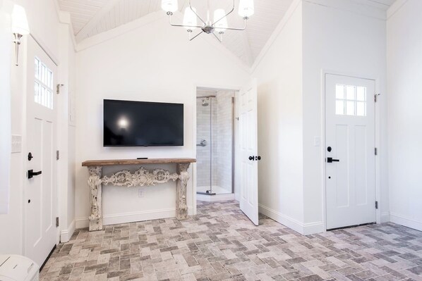 A hallway with a television mounted on the wall, a wooden console table, and a herringbone-patterned floor.
