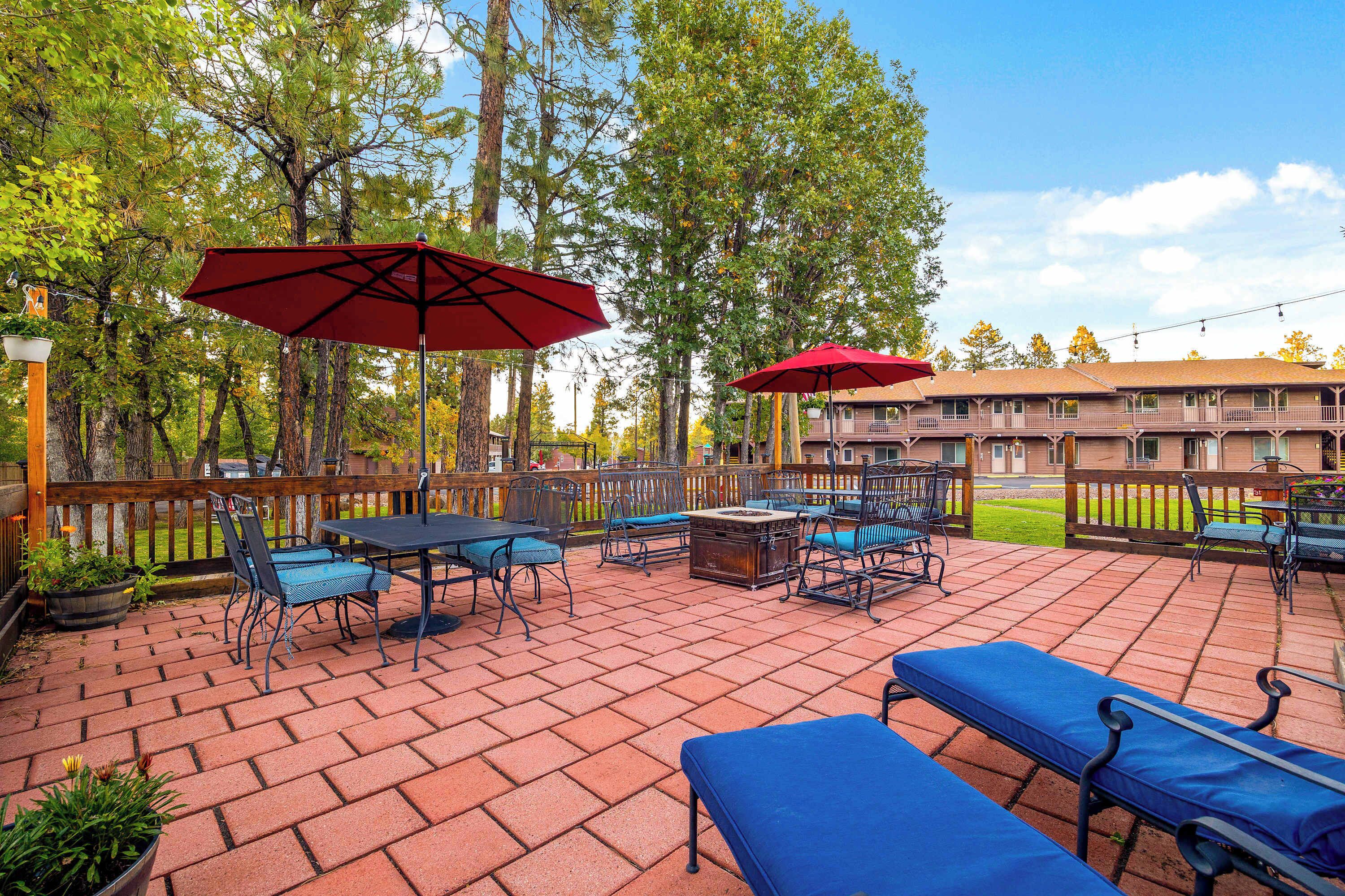 Ein Patio mit Außenbestuhlung, darunter Tische und Stühle, und zwei rote Sonnenschirme.