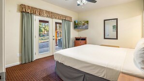 Een hotelkamer met een bed, een plafondventilator, een televisie, een spiegel en uitzicht op het omliggende landschap door de deur.