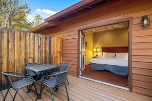 En stuga av trä med en balkong, en säng med en sänggavel, två stolar och ett bord.