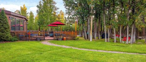 A park with a wooden deck, red umbrellas, and picnic tables.