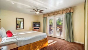 Quarto de hotel com cama, ventoinha no teto, televisão e porta de vidro deslizante para área externa.