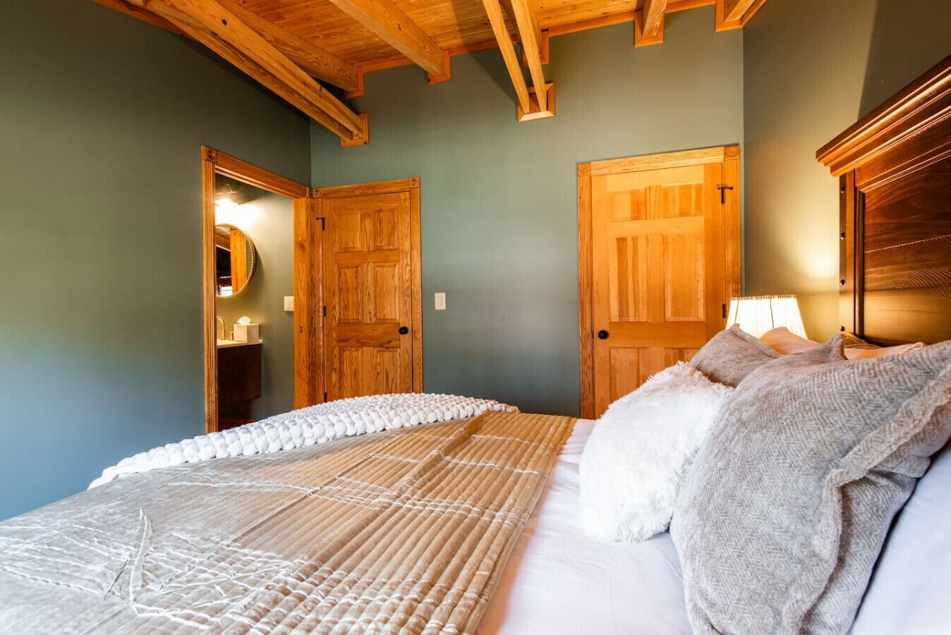 Een slaapkamer met een houten plafond, twee houten deuren, een bed met witte beddengoed en een bedlampje.