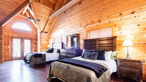 Ein Schlafzimmer in einer Blockhütte mit zwei Betten, Holzwänden, einer geneigten Decke und einem großen Fenster.