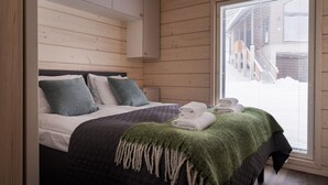 Ein Schlafzimmer mit Bett, Kissen, einem Nachttisch, einem Fenster mit Jalousien und Blick auf ein Gebäude.