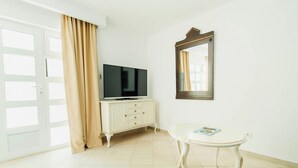 A room with a television on a white cabinet, a small white table, and a large mirror on the wall. - Yellow 1-bedroom apartment with AC in vibrant Budva (Budva)