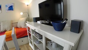 A bedroom with a bed, a TV, a white cabinet with shelves, and a lamp. - DiscoverHome Sacramento (Cádiz)