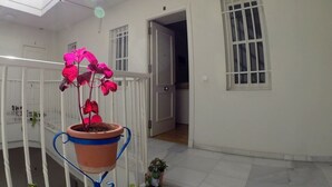 A room with a potted plant on a stand, a door leading to another room, and a window with bars. - DiscoverHome Sacramento (Cádiz)