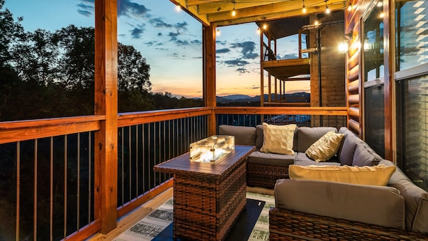 Eine Holzterrasse mit Feuerstelle, Korbmöbeln und großen Fenstern mit Blick auf die Landschaft.