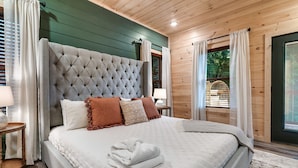 Ein Schlafzimmer mit einem großen, gepolsterten Kopfteil, einem ordentlich bezogenen Bett und Blick ins Freie durch ein Fenster.