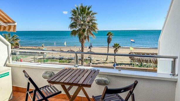 A balcony with a wooden table and chairs, overlooking a beach with palm trees and flags. - Studio in Torremolinos by Playa El Bajondillo (Torremolinos)