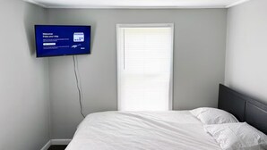 Een hotelkamer met een bed, een aan de muur bevestigde televisie en een raam met zonwering.