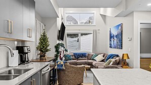 Une cuisine moderne équipée d’un four encastré, d’une machine à café et d’un petit sapin de Noël. On y trouve également un coin salon avec un canapé, une table basse et un téléviseur.