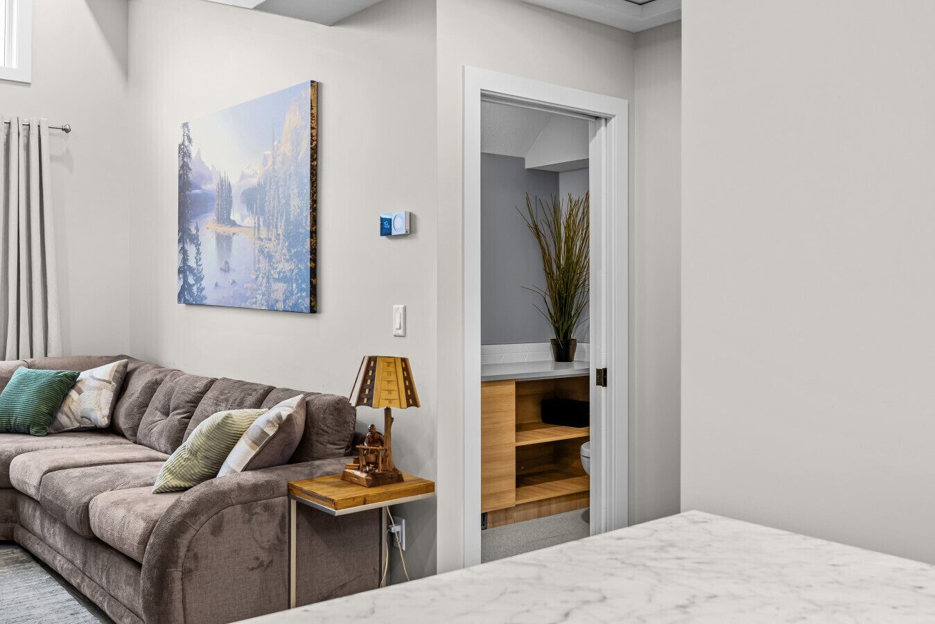 Un salon moderne avec un canapé, une table d’appoint, une lampe et un tableau accroché au mur.
