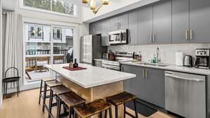 Une cuisine moderne avec des meubles gris, un îlot central et une grande fenêtre donnant sur un balcon.