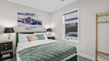 Une chambre à coucher avec un lit, deux tables de chevet avec des lampes, une fenêtre donnant sur un beau paysage et une étagère fixée au mur.