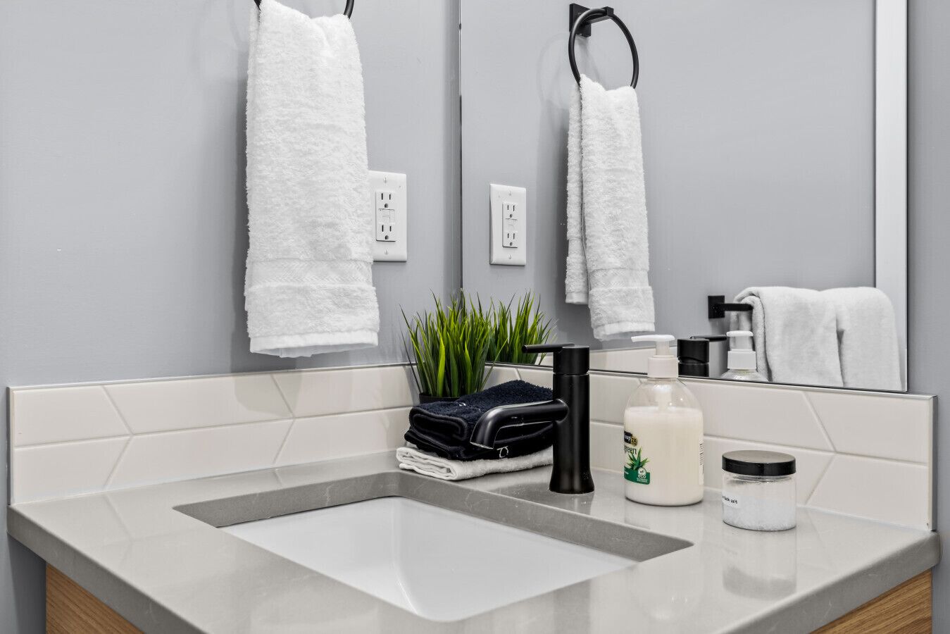 Un baño moderno con un espejo grande, toallas blancas, un grifo negro y una pequeña planta en la encimera.