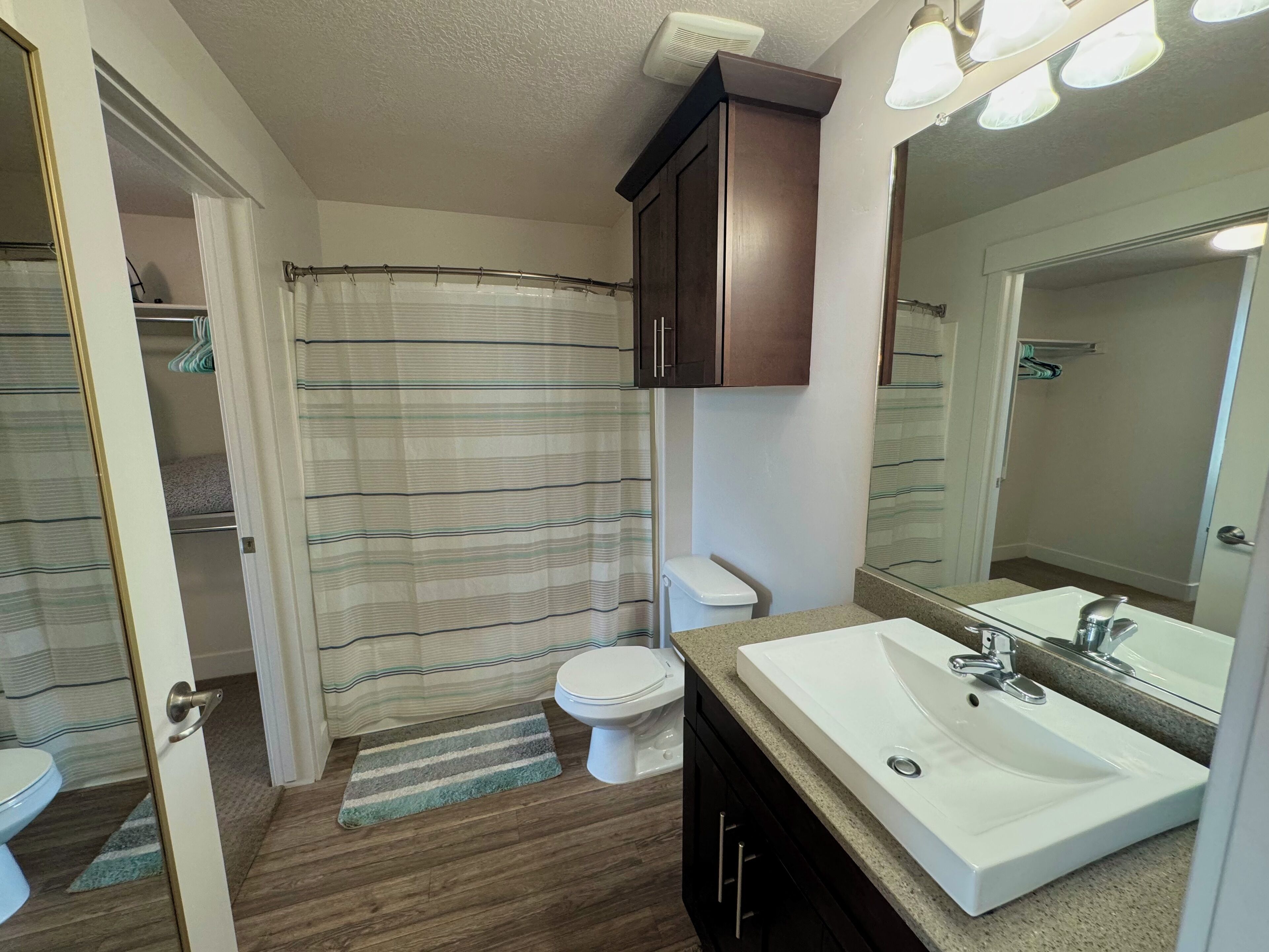 A bathroom with a shower curtain, toilet, sink, and mirror.