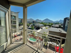 A balcony with a view of a swimming pool, a gas station, and mountains in the background. - Downtown Condo with Great Mountain Views (Salt Lake City)