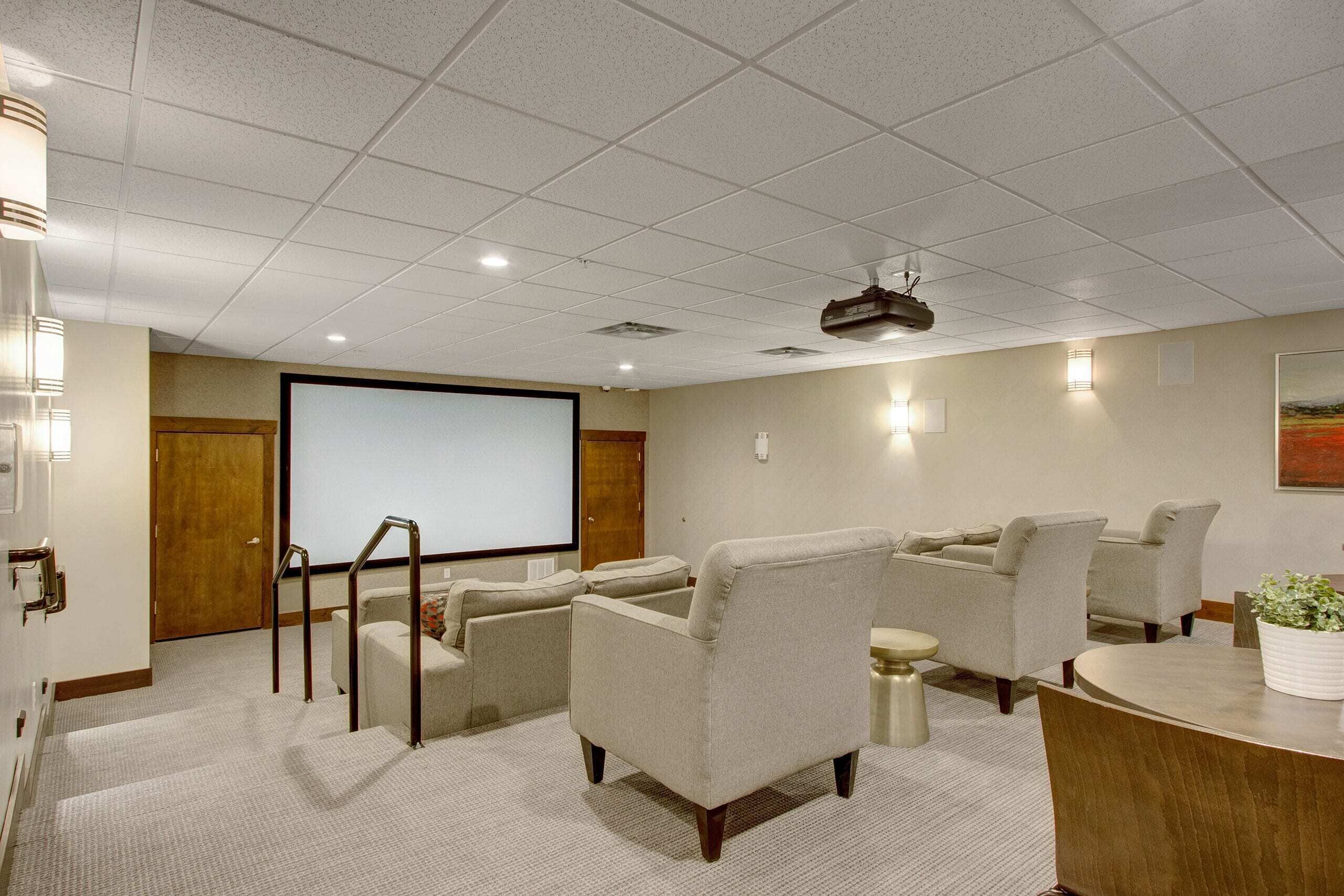 A conference room with a large screen, comfortable seating, a small table, and a staircase.