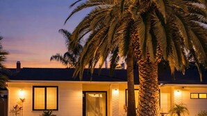 Una casa moderna amb un vestíbul ben il·luminat, una palmera gran i un jardí ben cuidat.