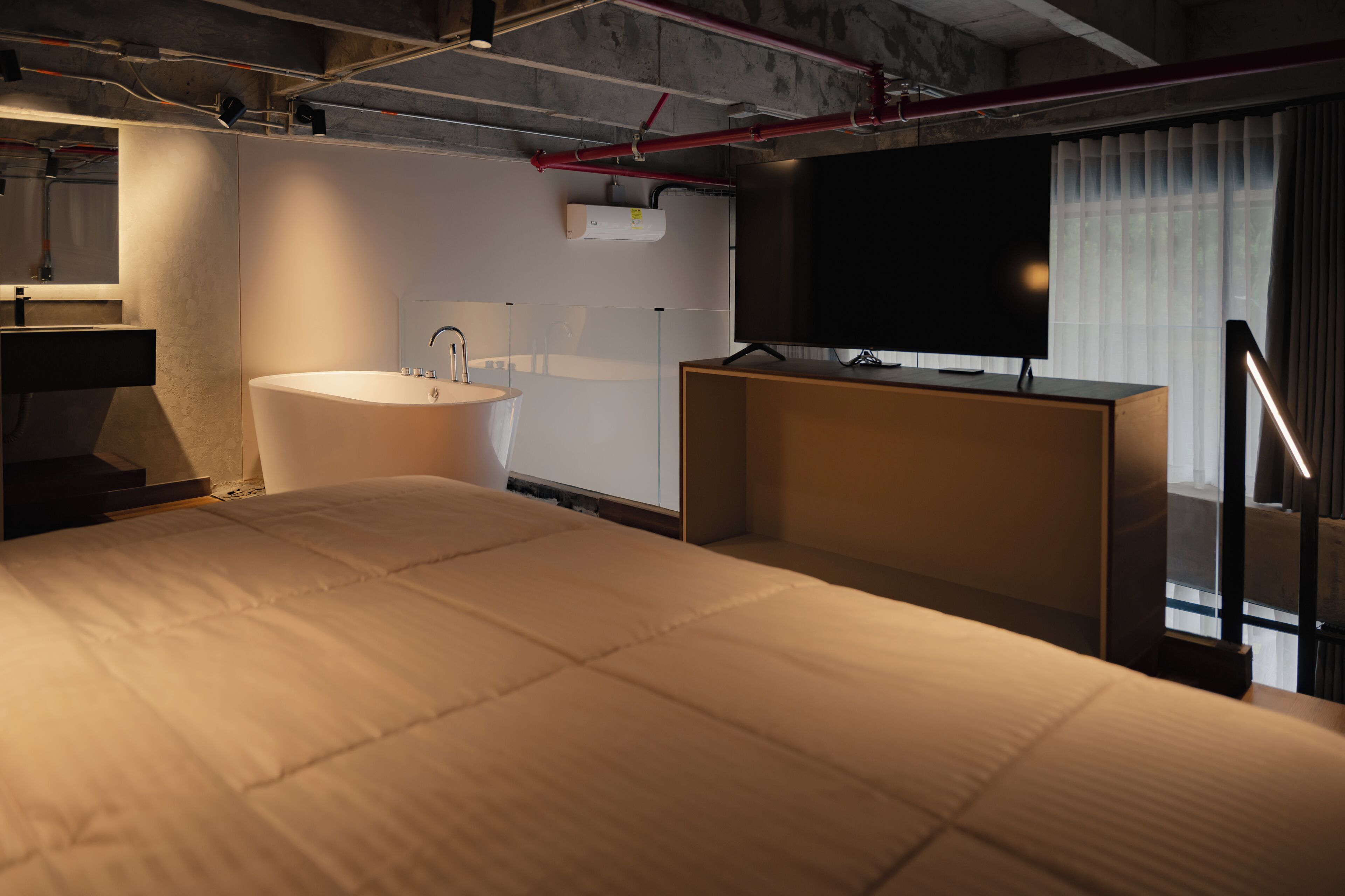 A modern hotel room with a large bed, a built-in bathtub, a vanity with a mirror, and a flat-screen TV.
