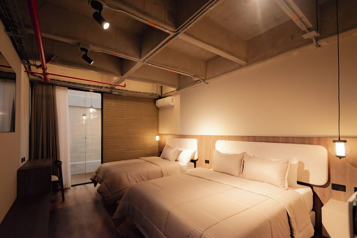 Ein Hotelzimmer mit zwei Betten, einem Schreibtisch und einer Schiebetür zum Balkon.