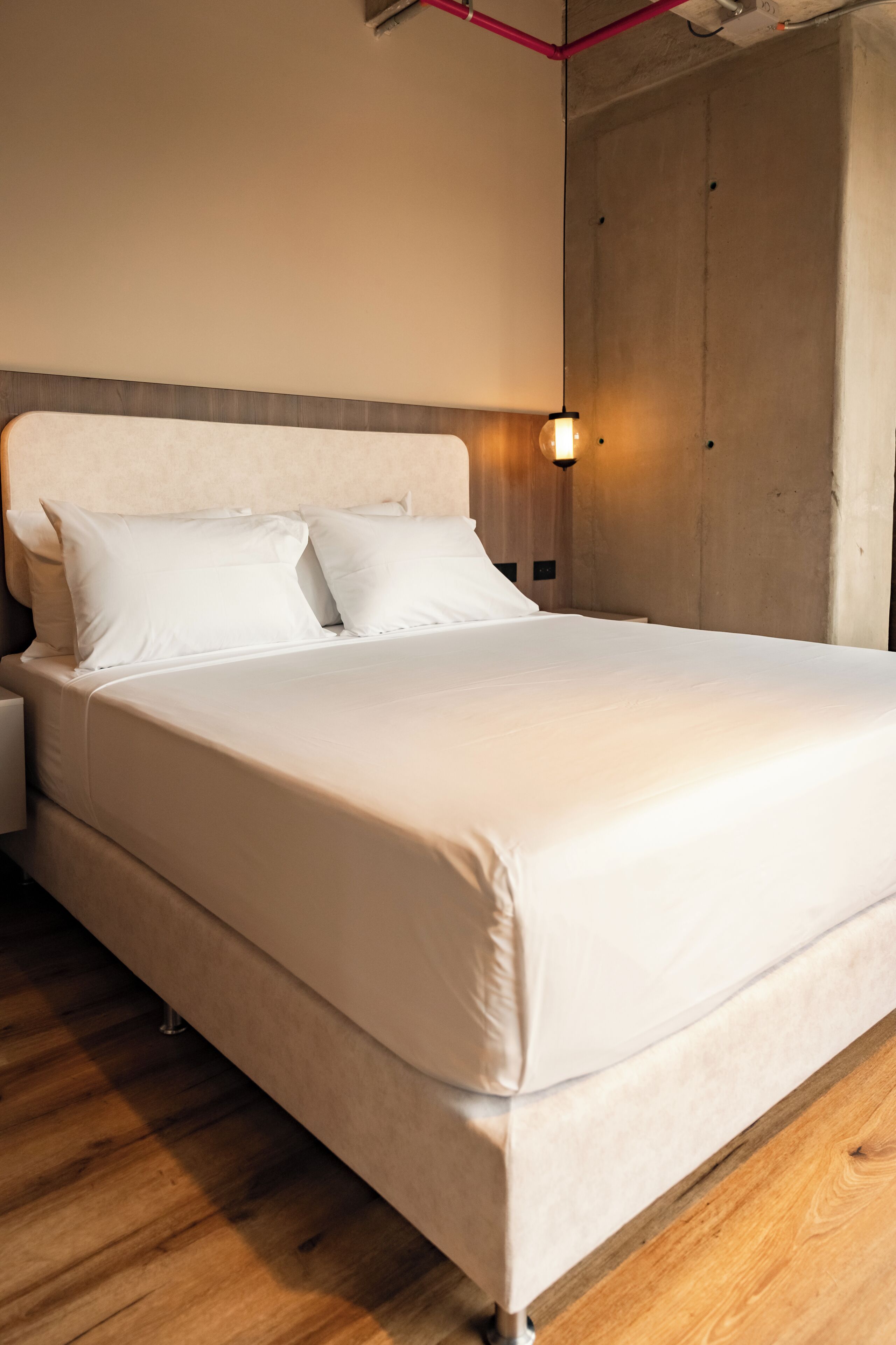 A neatly made bed with white linens in a modern room with wooden flooring and a concrete accent wall.