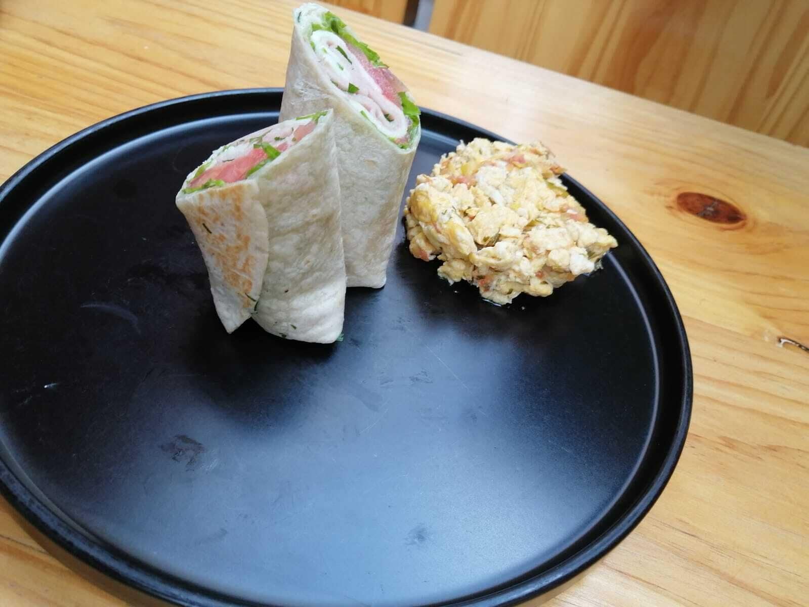 A black plate with a sandwich and a side dish on a wooden table.