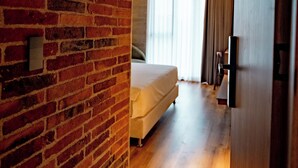 Habitación de hotel con pared de ladrillo, suelo de madera, cama y puerta que da a otra habitación.