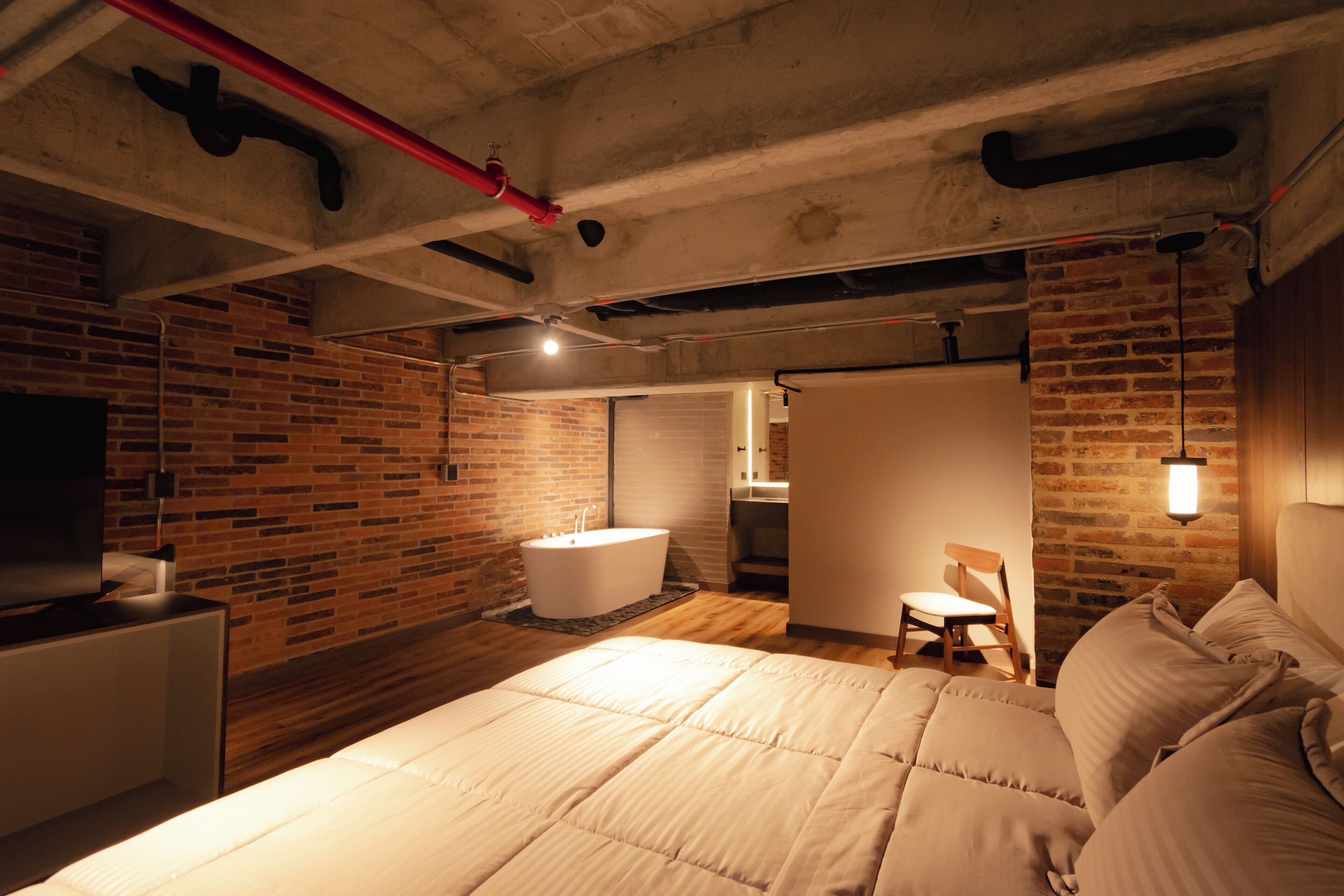 Ein modernes Schlafzimmer mit einem großen Bett, einer Ziegelwand, einer Badewanne und einem Fernseher.
