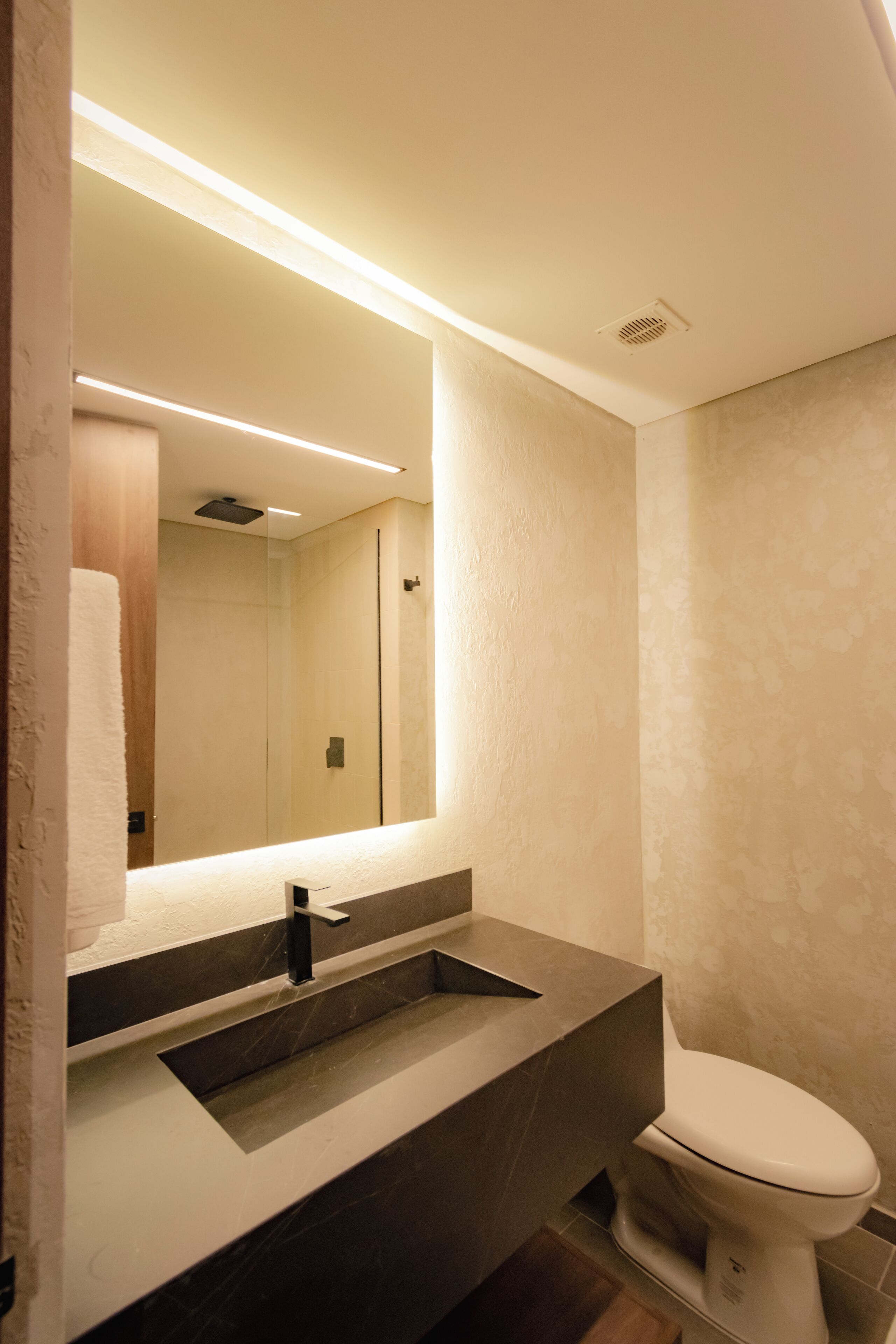 Un baño moderno con un espejo grande, un lavabo y un inodoro.