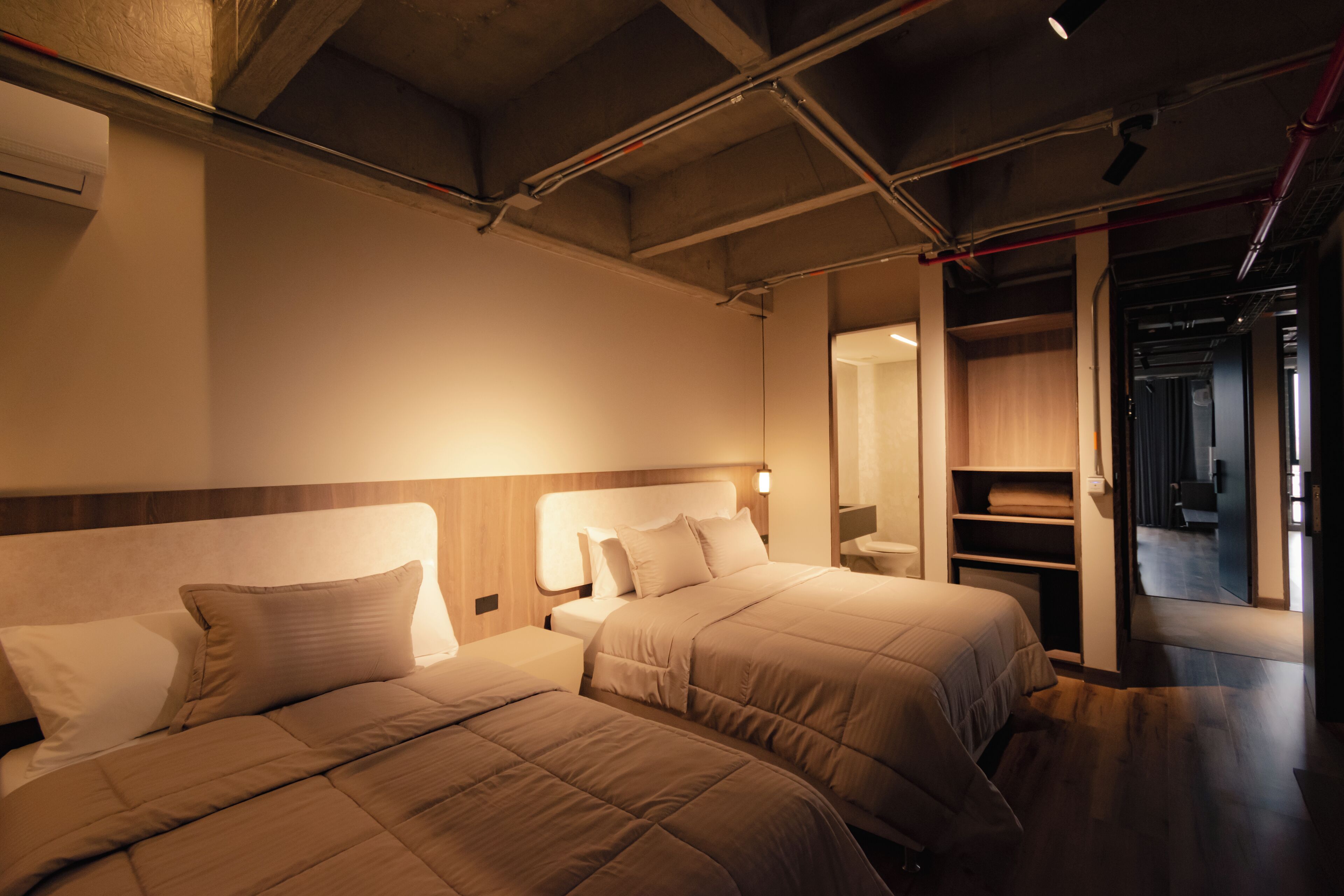 Une chambre d’hôtel avec deux lits, une tête de lit en bois, une table de chevet et un dressing.