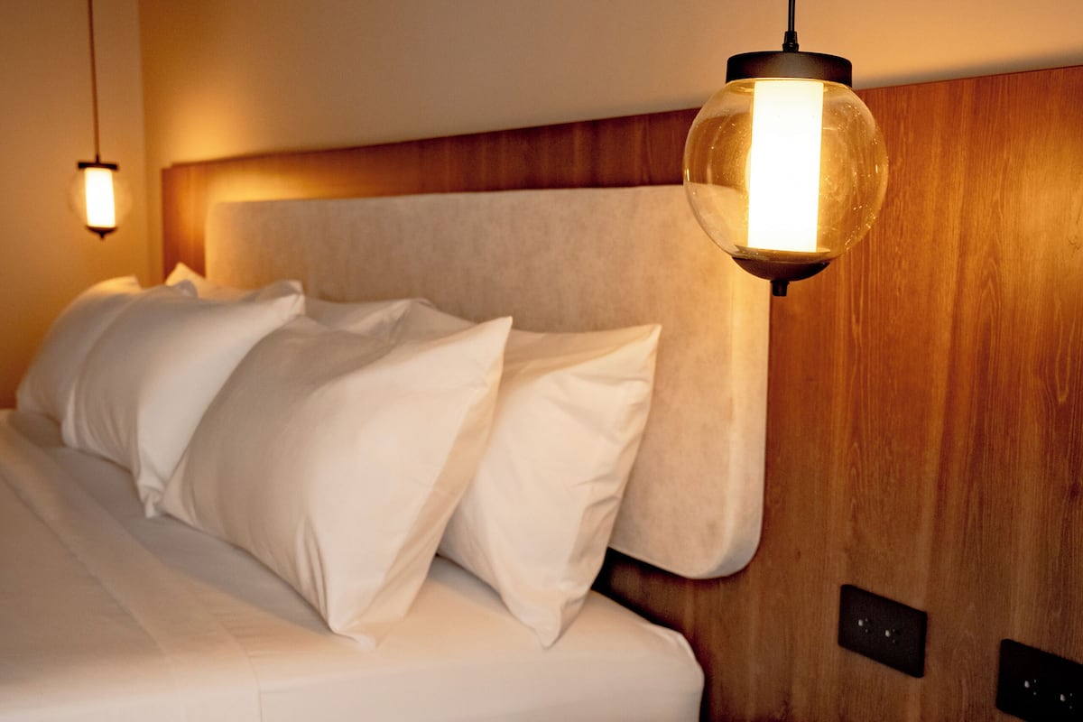Ein modernes Schlafzimmer mit einem hölzernen Kopfteil, einem weißen Bett mit vielen Kissen und einem Nachttisch.