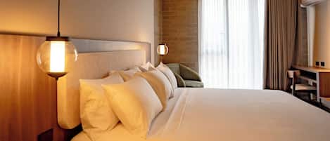 A hotel room with a large bed, two bedside lamps, a wooden headboard, a brick wall, and a window with curtains.