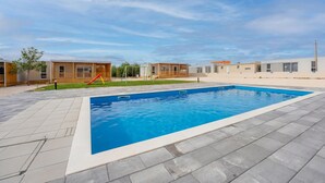 A swimming pool with a tiled deck, surrounded by modern buildings with wooden decks and a playground. - PREMIUM HOLIDAY HOUSE 3 (Privlaka)