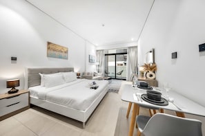 A modern hotel room with a bed, bedside table, lamp, and a dining area with a table set for two. - Stayshort - Modern Studio in Production City Sleeps 3 (Dubai)