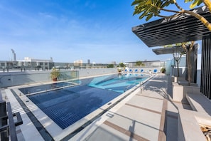 A rooftop swimming pool with clear blue water, surrounded by lounge chairs and a pergola. - Stayshort - Modern Studio in Production City Sleeps 3 (Dubai)