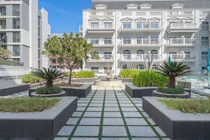 Ein modernes Hotel mit einem zentralen Innenhof, der eine Fontäne, Pflanzenkübel mit Grünpflanzen und einen gefliesten Weg umfasst.