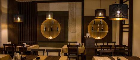 Un restaurant avec des tables rondes, des lambris en bois foncé et des lampes suspendues.