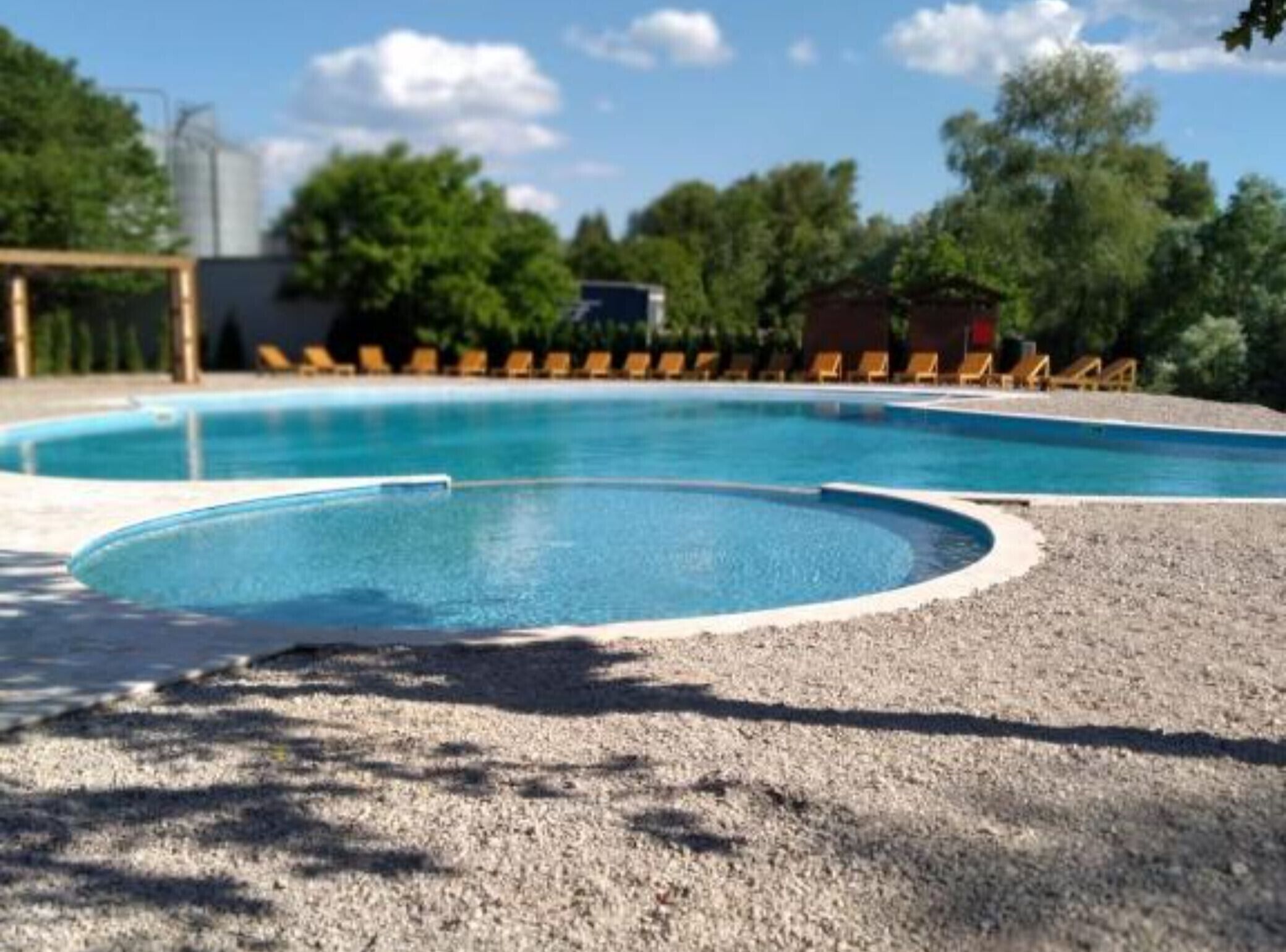 Una piscina con solárium de grava y sillones de descanso al fondo.